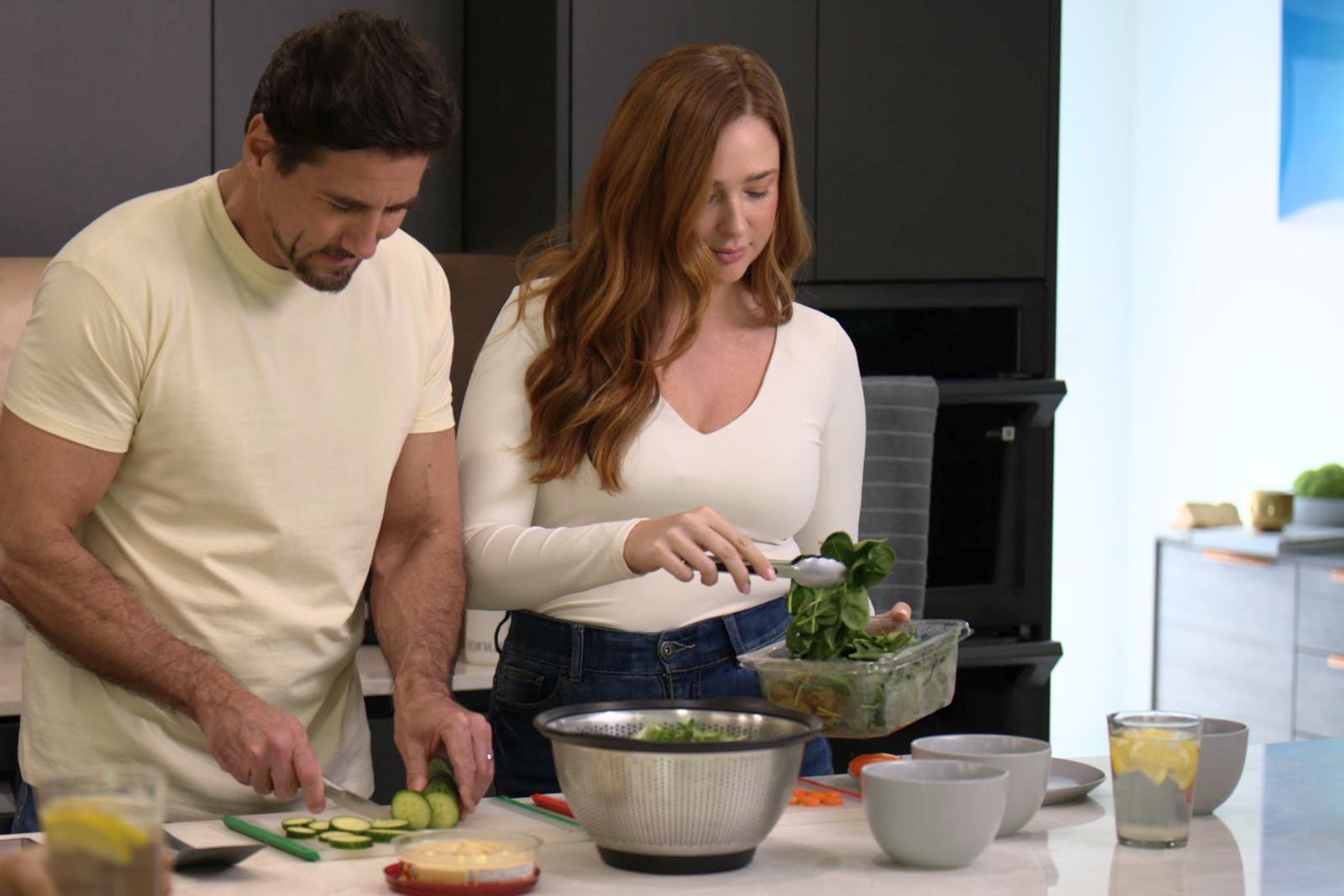 man and woman in modern kitchen slicing vegetables for salad