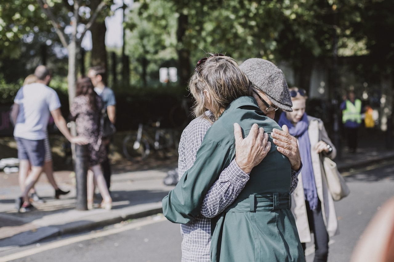 elderly woman hugging man on pavement near park