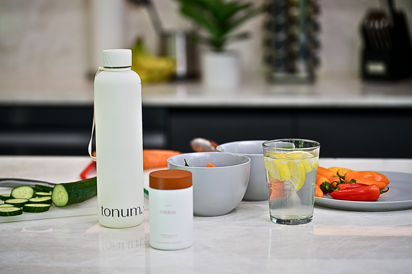 tonum branded water bottle and motus supplements on a counter beside vegetables and beverages