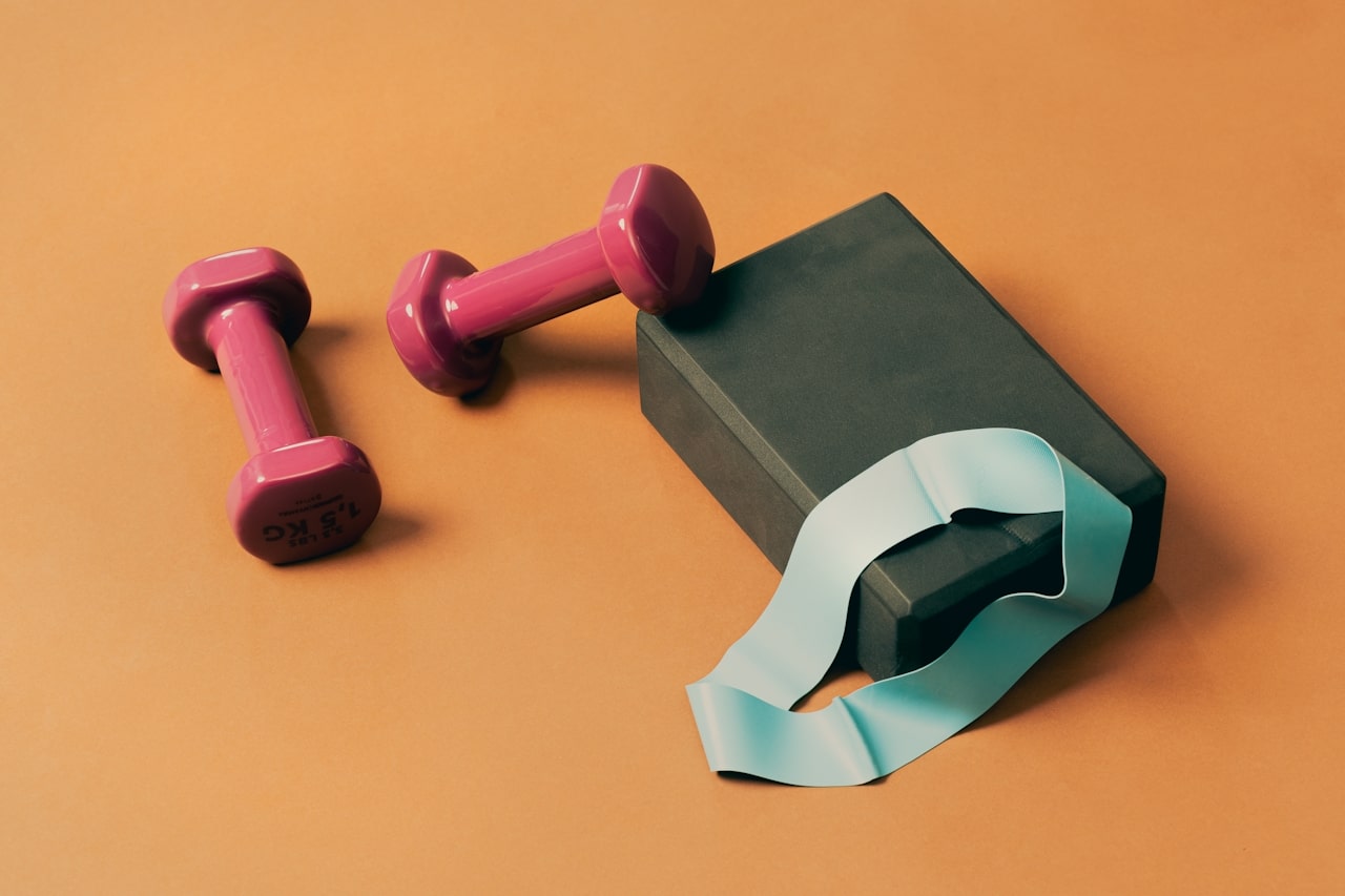 pink dumbbells placed next to yoga block and resistance band