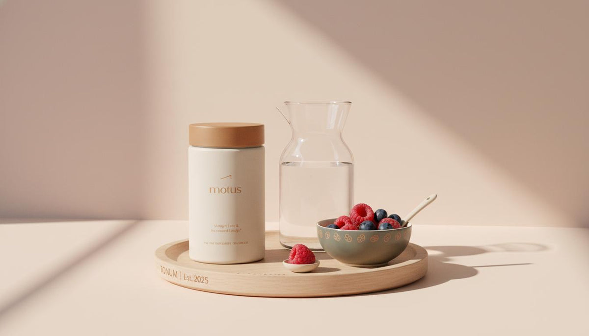 Minimalist kitchen countertop with a Tonum Motus supplement jar on a wooden tray beside a carafe of water and bowl of berries, conveying l-carnitine wellness and calm lifestyle.