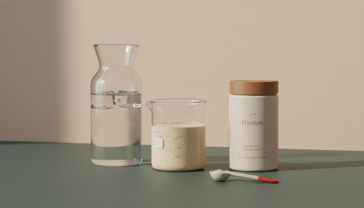 Minimalist still-life of a carafe, thick protein-fiber smoothie in a lab beaker, and Motus supplement container on a beige backdrop — best drink to curb your appetite