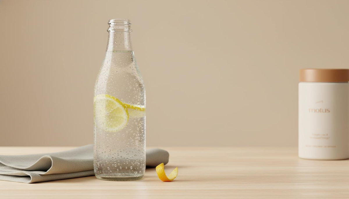 Minimalist photo of chilled sparkling water with lemon slices on a light wooden table and a Tonum Motus supplement container in the background, emphasizing hydration for fatty liver