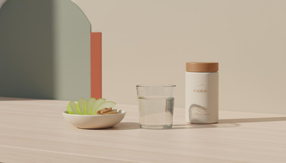 Minimalist still-life of water, apple slices with almond butter and a Tonum Motus jar on a wooden counter illustrating practical tools for how to lessen cravings.