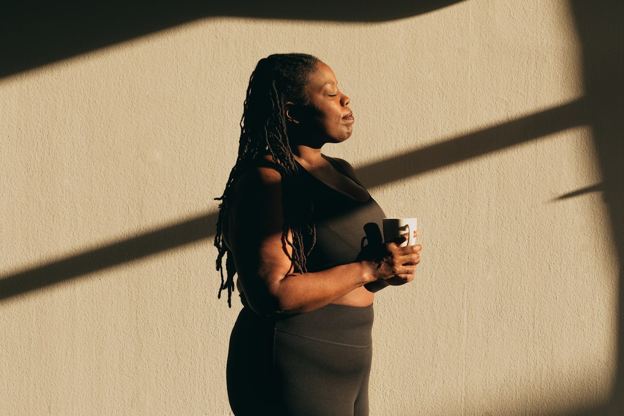 woman wearing athleisure closing eyes and holding mug while standing