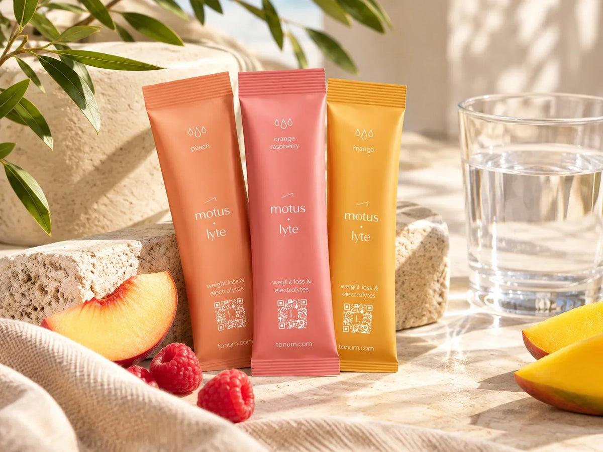 Tonum Motus Lyte electrolyte sachets in peach, orange raspberry, and mango beside a glass of water, with fresh fruit in a warm sunlit setting.
