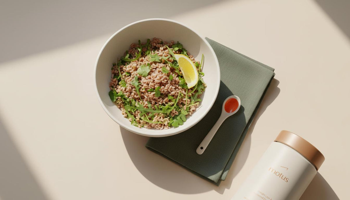 Minimalist chilled grain bowl with arugula, herbs and lemon wedge and Tonum Motus container at the edge — plants that increase GLP-1 healthy food concept.