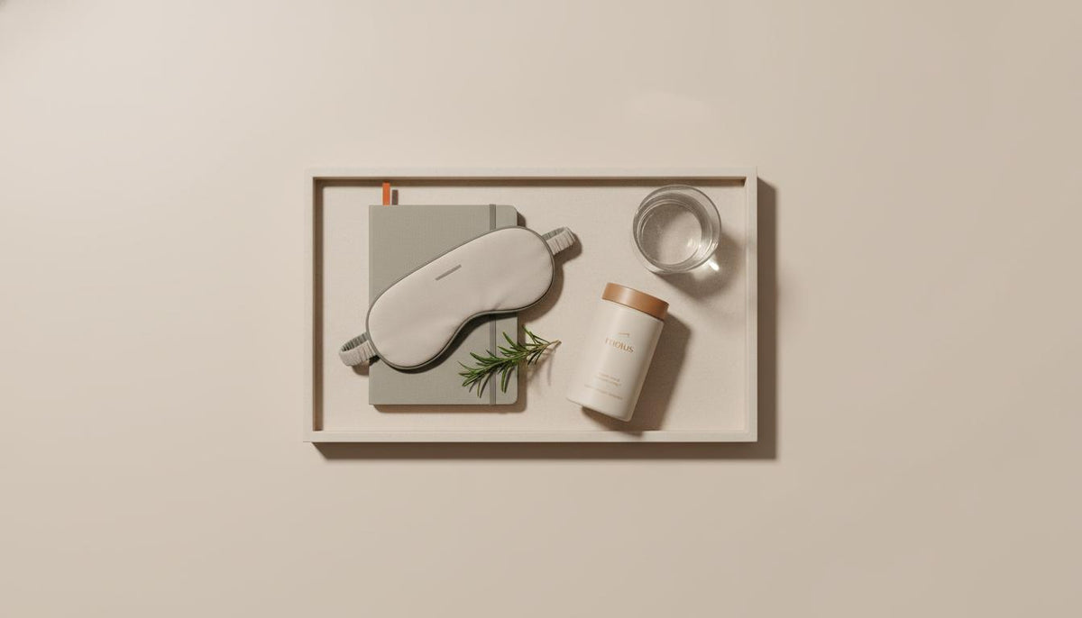 Minimalist flat-lay of a tray with a closed notebook, sleep mask, Tonum supplement container, rosemary sprig and glass of water on a #F2E5D5 background, evoking routine for serotonin depletion.