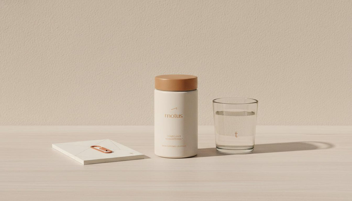 Minimalist still-life of Tonum Motus supplement jar on light wood with notepad and glass of water against #F2E5D5 background — what is the best prescription appetite suppressant pill?