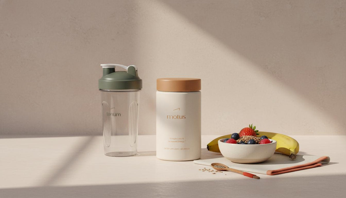 Minimalist still life of Tonum Motus container beside a clear shaker bottle and a bowl of berries, a banana, and seeds on a beige countertop — what shake is best for losing weight